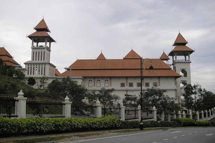 A large white building with multiple towers and a red roof, surrounded by a fence and greenery. 5