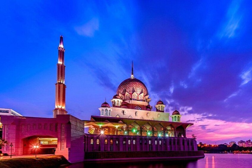 A mosque with a tall minaret and a large dome, illuminated at dusk. 1