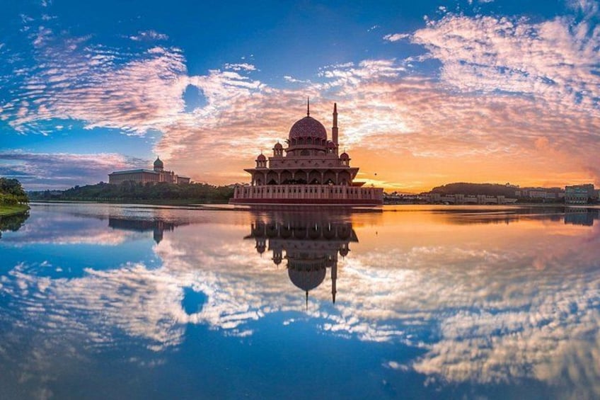 A mosque with a large dome and minarets, reflecting on a calm body of water, with a sunset sky in the background. 3