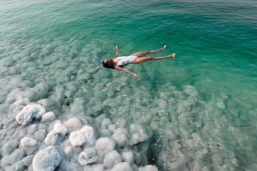 A person floating on clear turquoise water with visible underwater rocks and white formations. 1