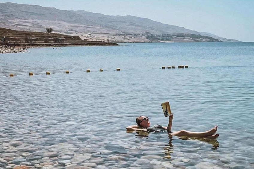 A person lying on a beach with a book, surrounded by calm water and distant mountains. 2
