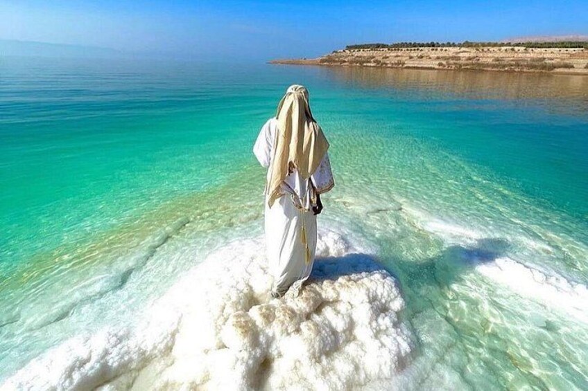A person standing on a white sandy beach with clear turquoise water. 4