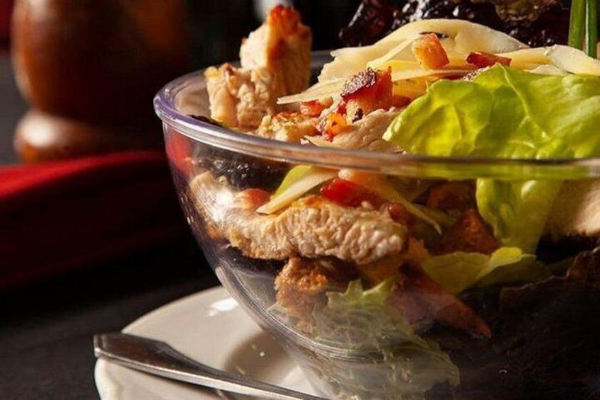 Een glazen schaal met een salade van sla, kip en rode paprika. 4