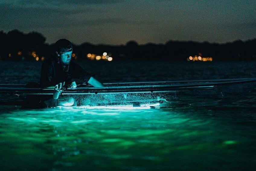 A person sitting on a boat at night with a green light on the water. 5