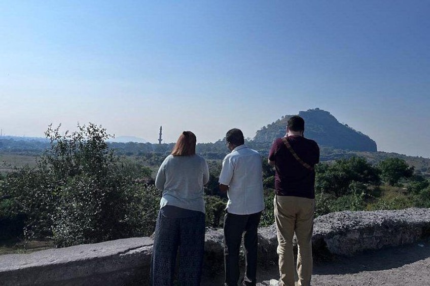 Drei Personen stehen auf einer Steinmauer und blicken auf eine Landschaft mit einem Hügel und einem Turm in der Ferne. 2