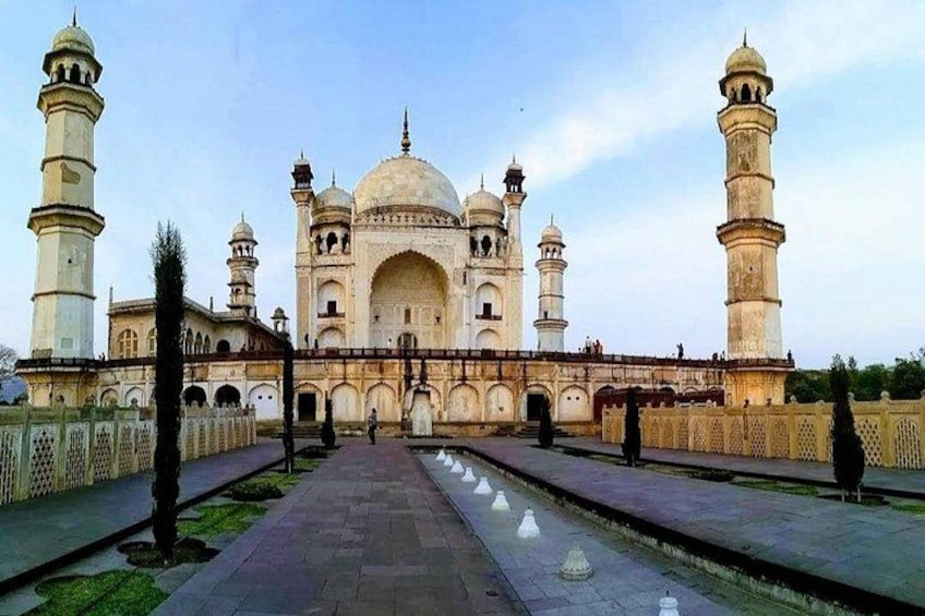 Ein großes, historisches Gebäude mit mehreren Kuppeln und Minaretten, umgeben von einem gepflasterten Weg und einem Wasserkanal. 3