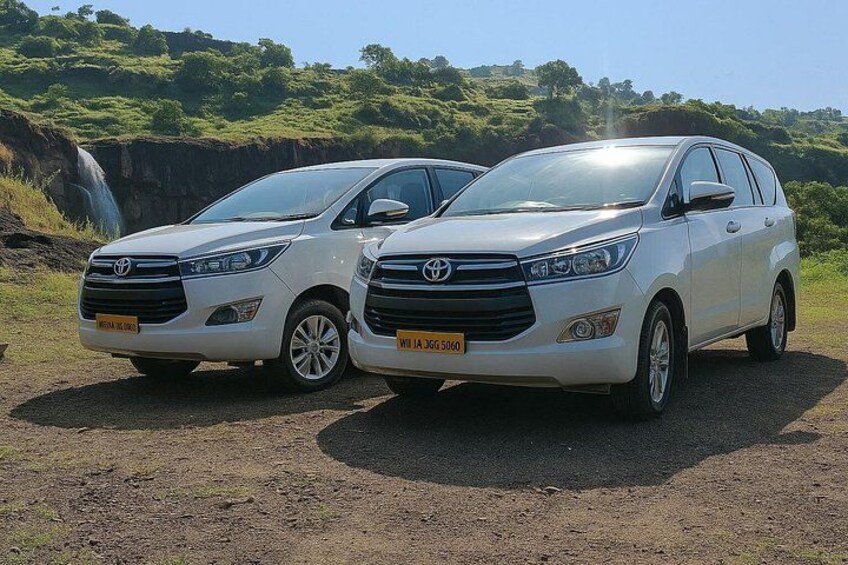 Deux SUV Toyota blancs sont stationnés sur un chemin de terre, avec une cascade et une végétation luxuriante en arrière-plan. 1