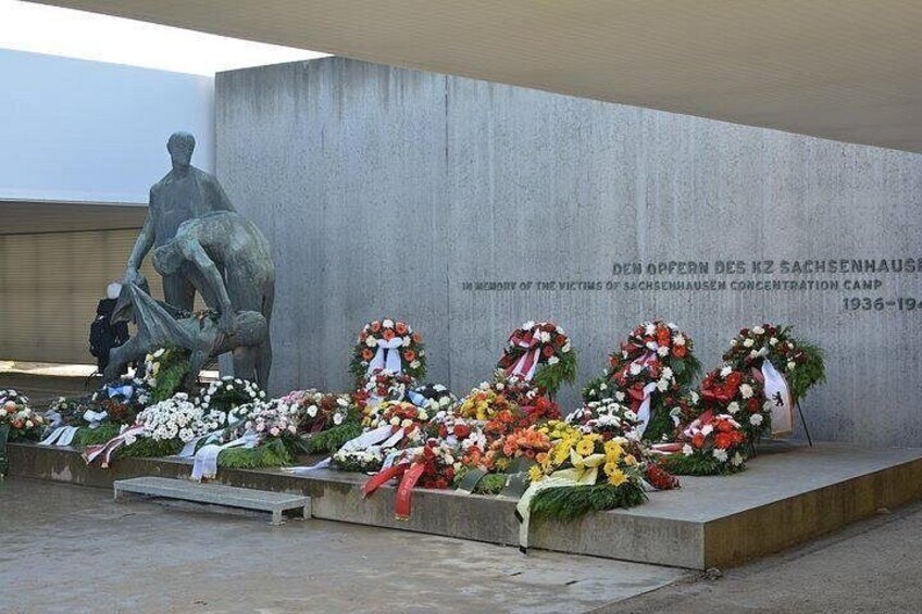 Un mémorial comprenant une statue, des fleurs et un mur portant une inscription. 4