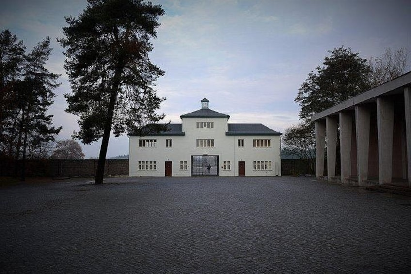 A white building with a symmetrical facade, a central entrance, and a paved courtyard. 2