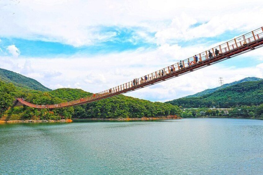 A long pedestrian bridge over a river, surrounded by lush green hills. 1