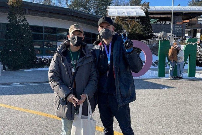Two people standing in front of a building with a large green 'M' sign. 4