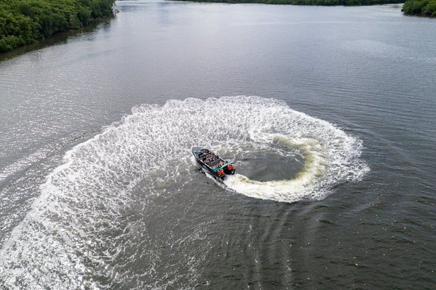 Ein Boot hinterlässt eine Wasserwelle in einem von Grünpflanzen gesäumten Fluss. 4