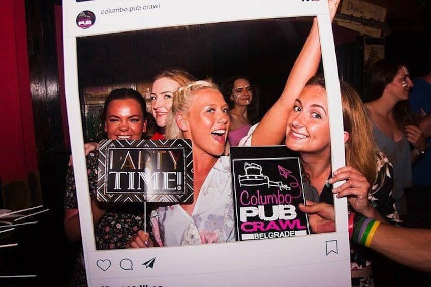 A group of people holding a photo booth with a sign that reads 'Columbo Pub Crawl Belgrade.' 1
