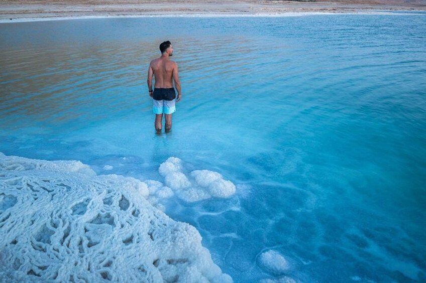 A person standing in clear blue water with a sandy beach in the background. 5