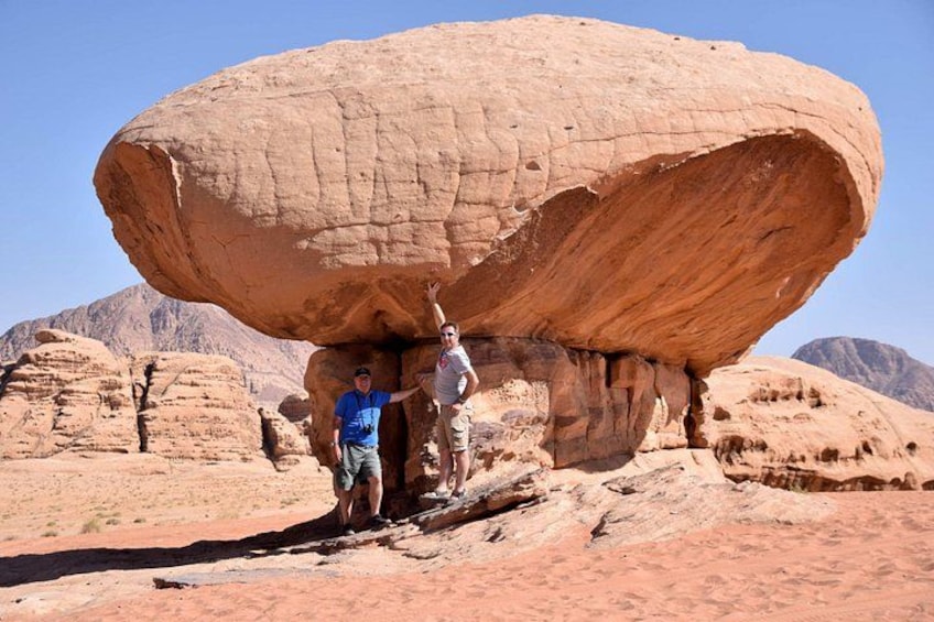 Two people standing under a large rock formation in a desert landscape. 2