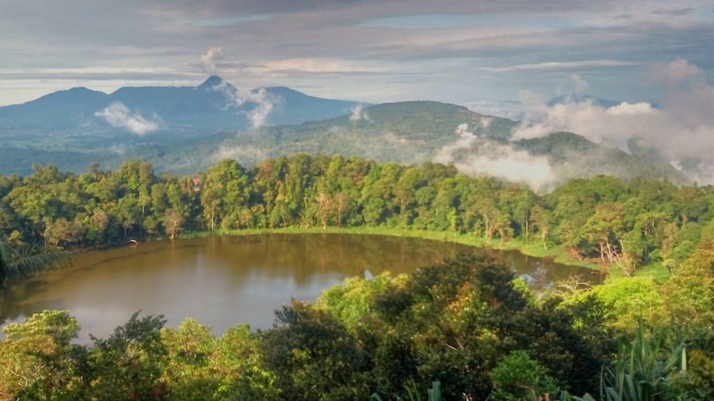 A lake surrounded by dense forest and mountains with visible smoke or steam rising from the peaks. 4