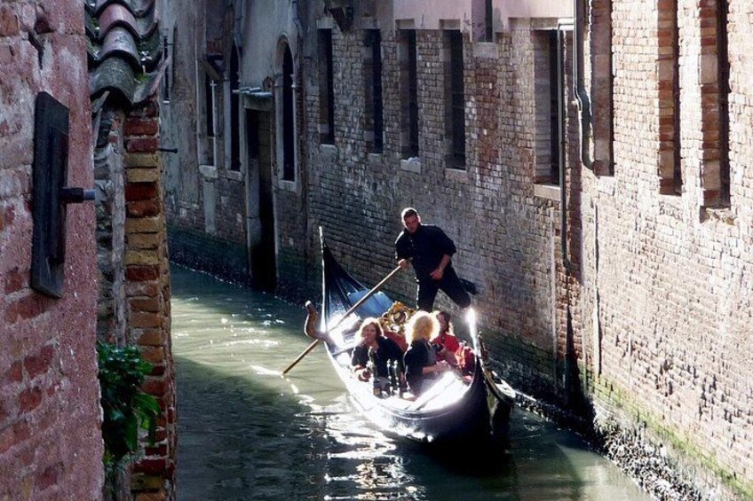 Un canal estrecho con una góndola transportando pasajeros, una persona remando y edificios a lo largo del canal. 2