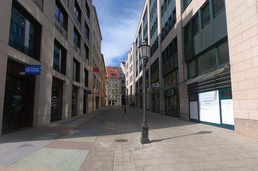 A pedestrian street lined with modern buildings, a street lamp, and a sign for a sports store. 4