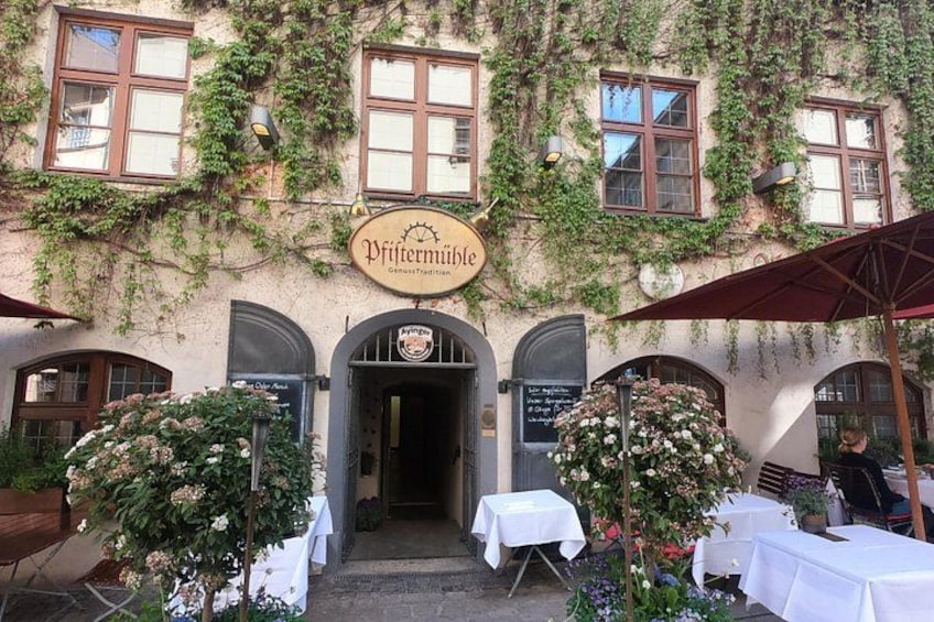 A building with ivy-covered walls, a sign reading 'Pflastermühle,' and tables set up outside for an event. 5