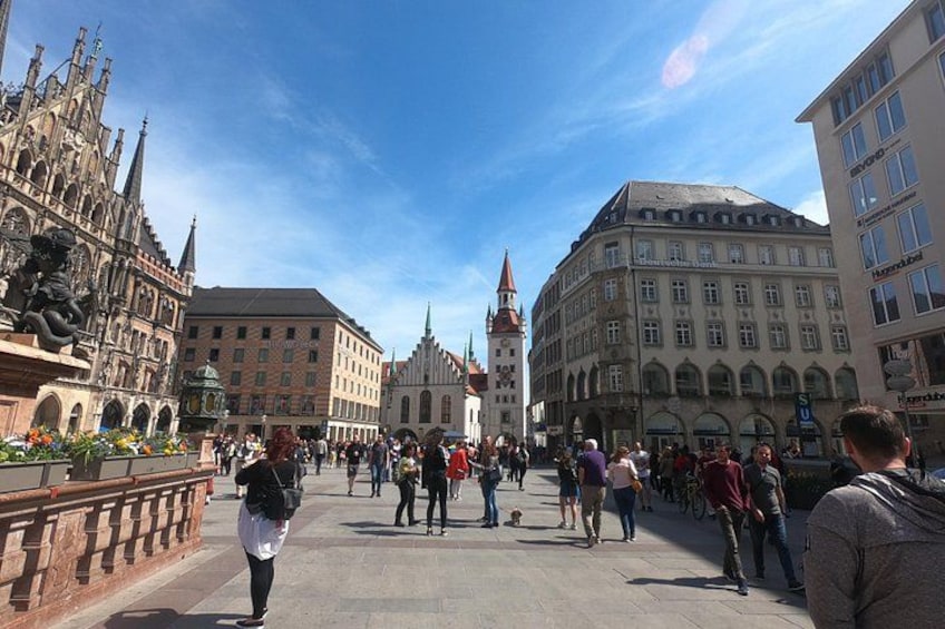 A busy square with historic buildings, a prominent church spire, and a statue. 2