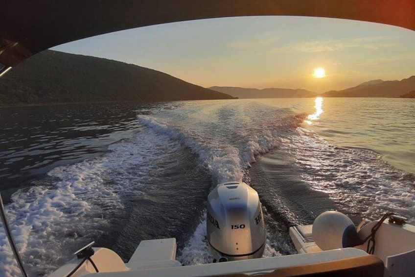 Un barco navegando en el agua, con estela y un sol poniéndose al fondo, y montañas a lo lejos. 3