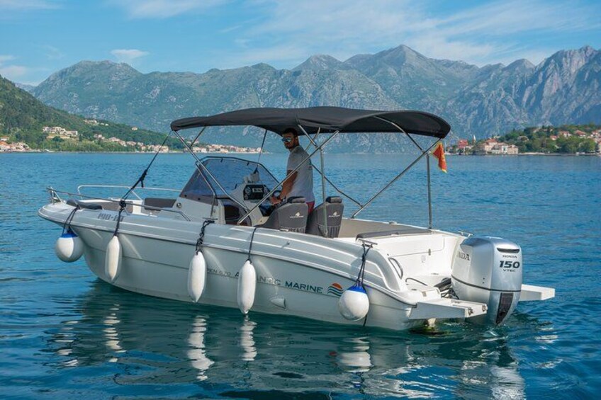 Un barco a motor blanco con toldo, con la leyenda "ANTIC MARINE", en un lago tranquilo con montañas al fondo. 4