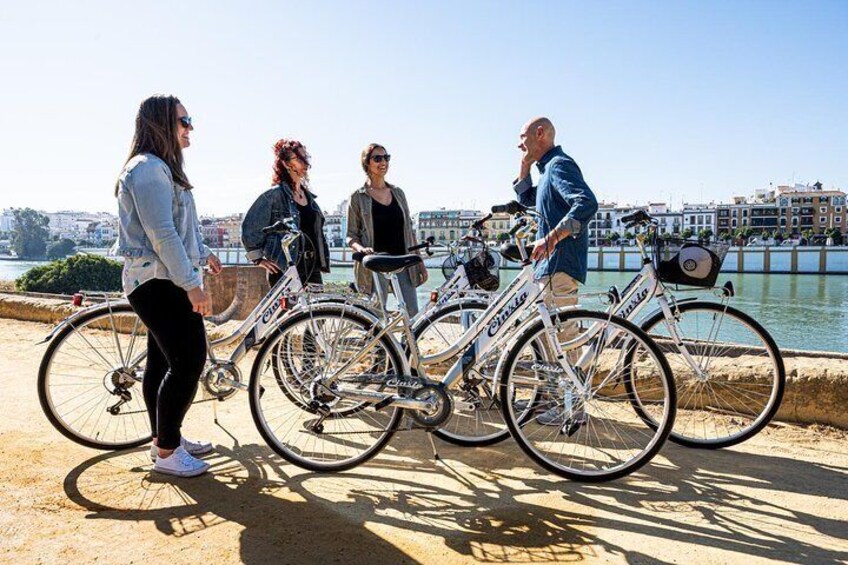 Four people standing by bicycles near a waterfront with buildings in the background. 5