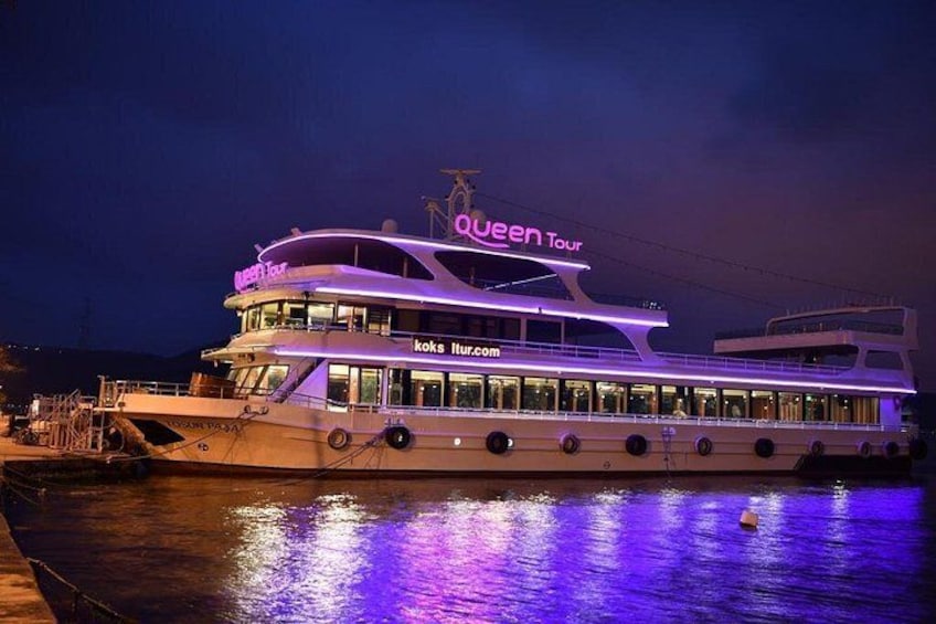 A large, illuminated boat with 'Queen Tour' written on the top, docked at night. 1