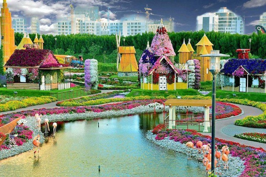 Un jardín colorido con un estanque, edificios fantásticos y un paisaje urbano al fondo. 3