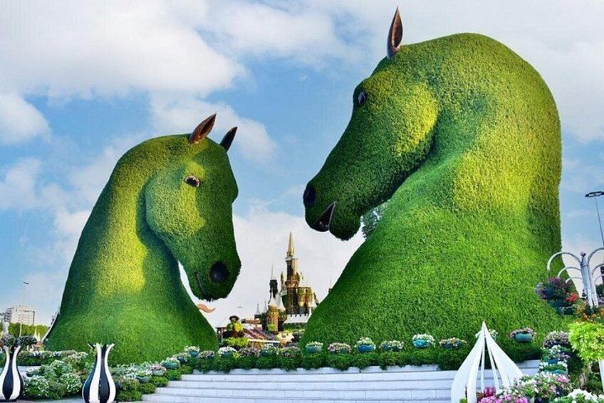 Una gran escultura de un caballo verde en un jardín con un castillo al fondo. 2
