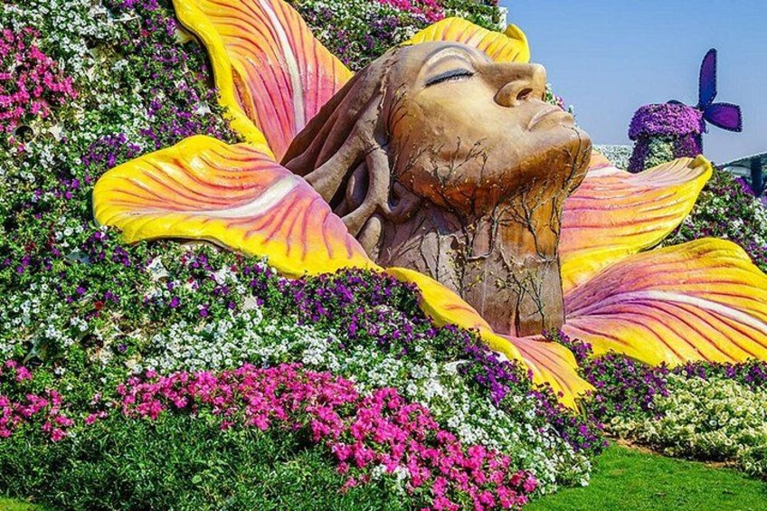 Una gran escultura floral con rostro, rodeada de flores y follaje de colores. 5