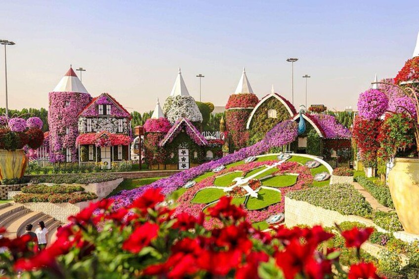 Un jardín con flores de colores, un reloj grande y edificios imaginativos. 4