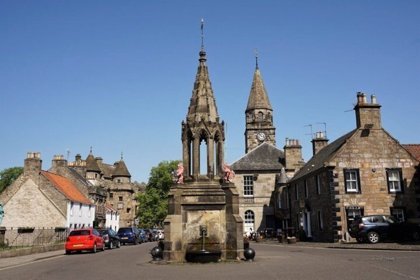 A historic town square with a prominent church tower, stone buildings, and a fountain. 1