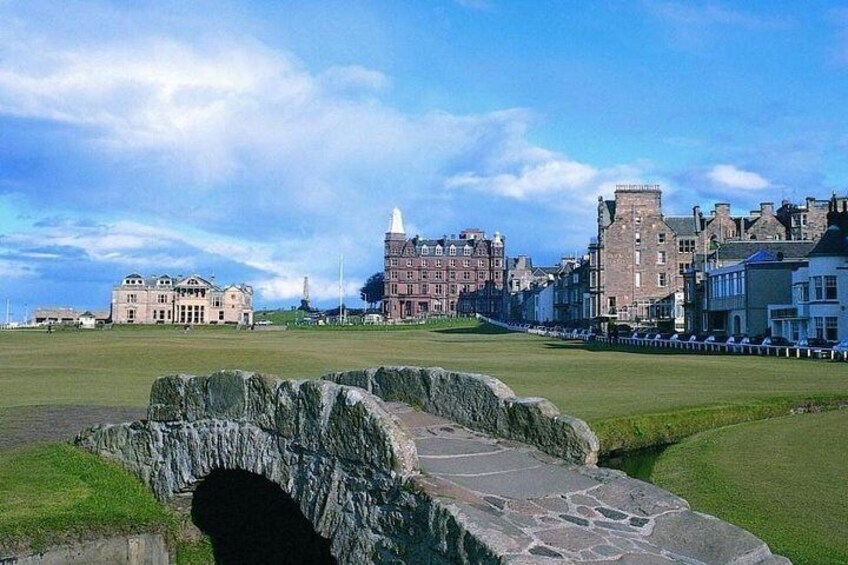 A stone bridge, a grassy field, and historic buildings in the background. 1