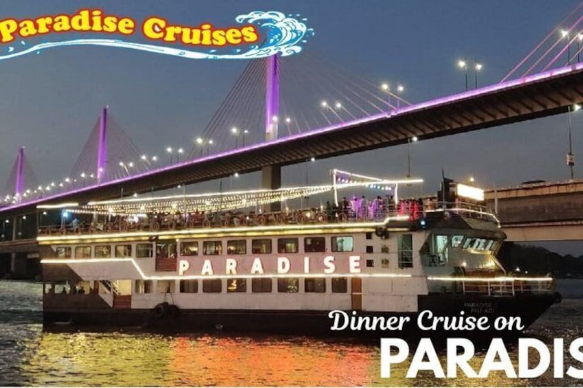 A cruise ship named 'PARADISE' with a deck area for dining, under a bridge with purple lighting. 1