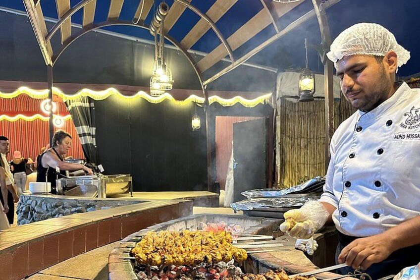 Un chef preparando comida en un evento al aire libre con un escenario y un público de fondo. 3