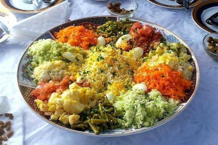 A large, ornate plate filled with various colorful food items, including rice, vegetables, and eggs, arranged on a tablecloth. 2
