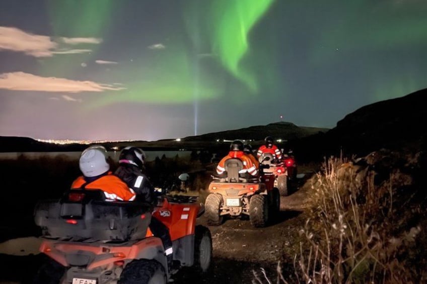 People on ATVs under a night sky with the Northern Lights. 4