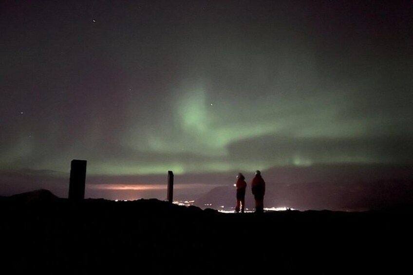 Two people standing on a hill, watching the northern lights. 5