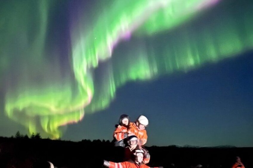 Una persona con un atuendo rojo y blanco y un casco, de pie bajo una exhibición de aurora verde. 2