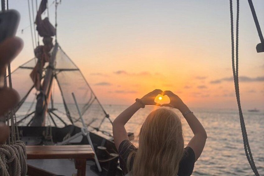 Une personne se trouve sur un bateau au coucher du soleil, et elle joint ses mains pour former un cœur, tandis que le soleil disparaît à l'horizon. 2