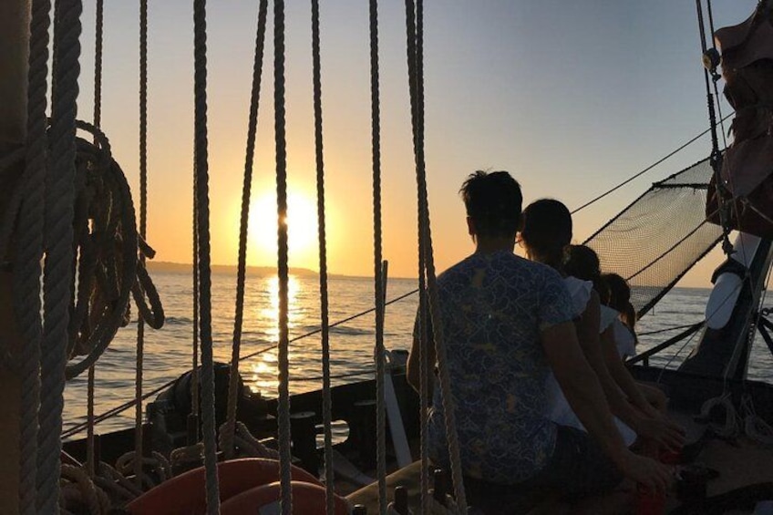 A sunset over the ocean with a sailboat and people on deck. 5
