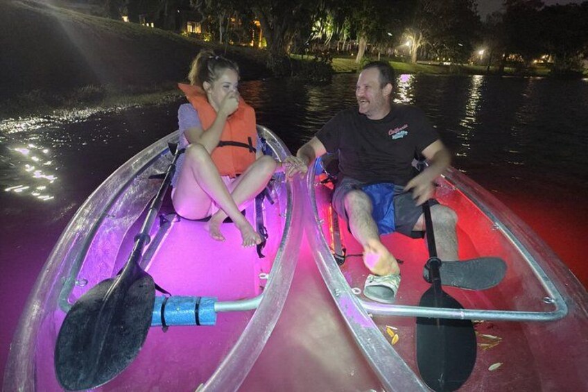 Two people in a transparent boat with a paddle, on a body of water at night. 4