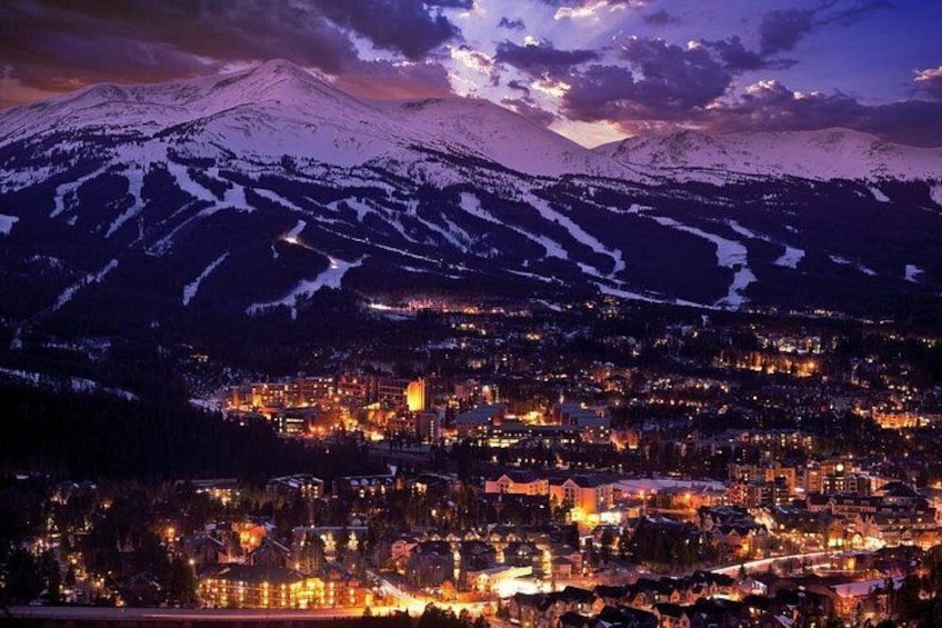 A snow-covered mountain at dusk with a town illuminated below. 5