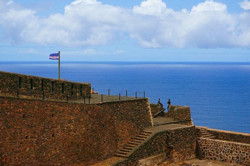 En stenvæg med et flag, en trappe og havet i baggrunden. 1