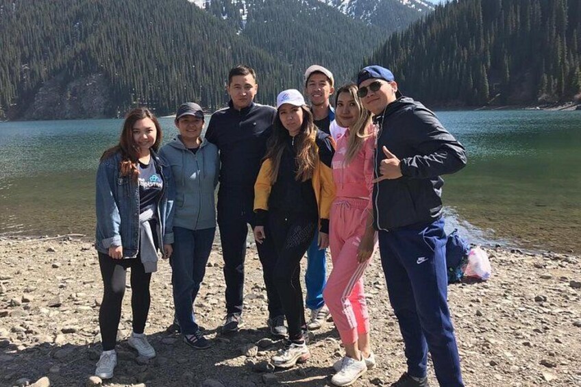 A group of people standing on a rocky shore with a lake and mountains in the background. 3
