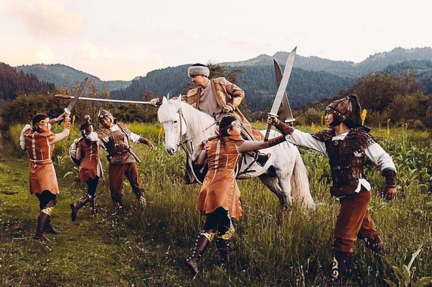 Un grupo de personas vestidas con trajes medievales en un campo de hierba con montañas al fondo. 1