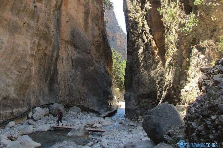 A canyon with a narrow stream, rocky terrain, and a person standing near the water. 4