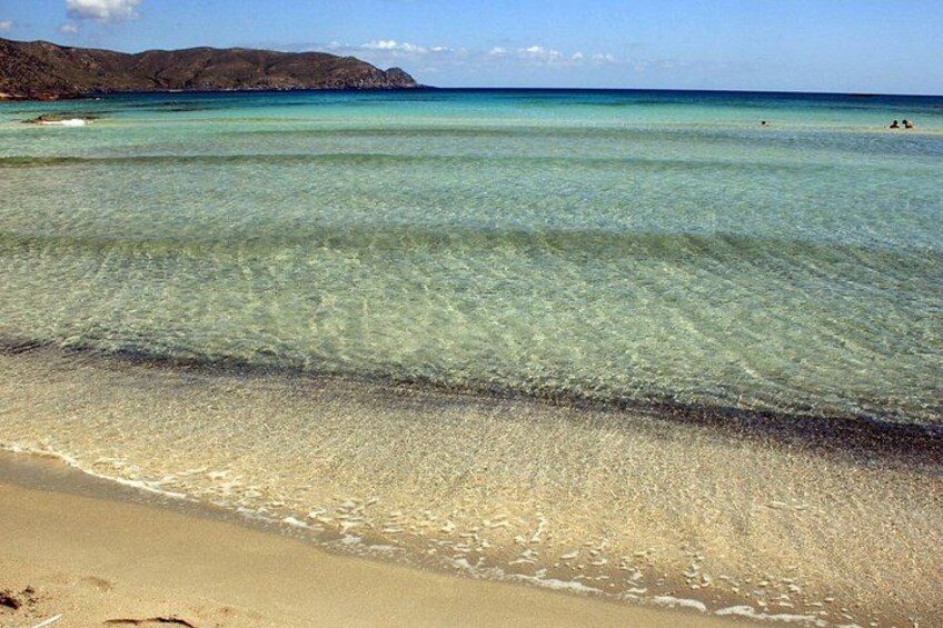 A beach with clear turquoise water, a sandy shore, and distant mountains. 5