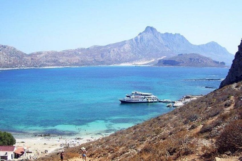 A coastal landscape with a boat docked near the shore, a beach, and mountains in the background. 4